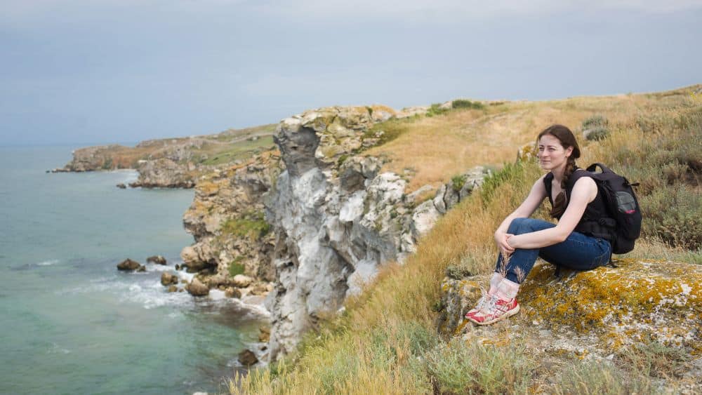 woman sits on the shore while hiking near the sea