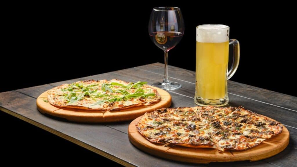 two pizzas and a glass of beer and red wine on a table mexita