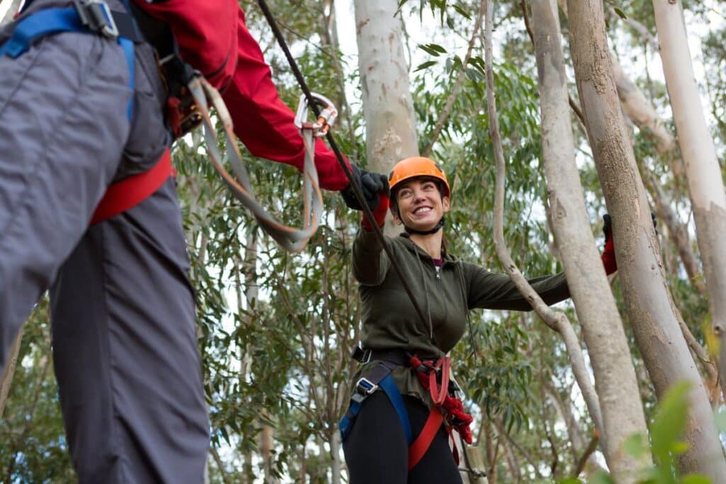 man helping woman to cross zip line in the forest during daytime