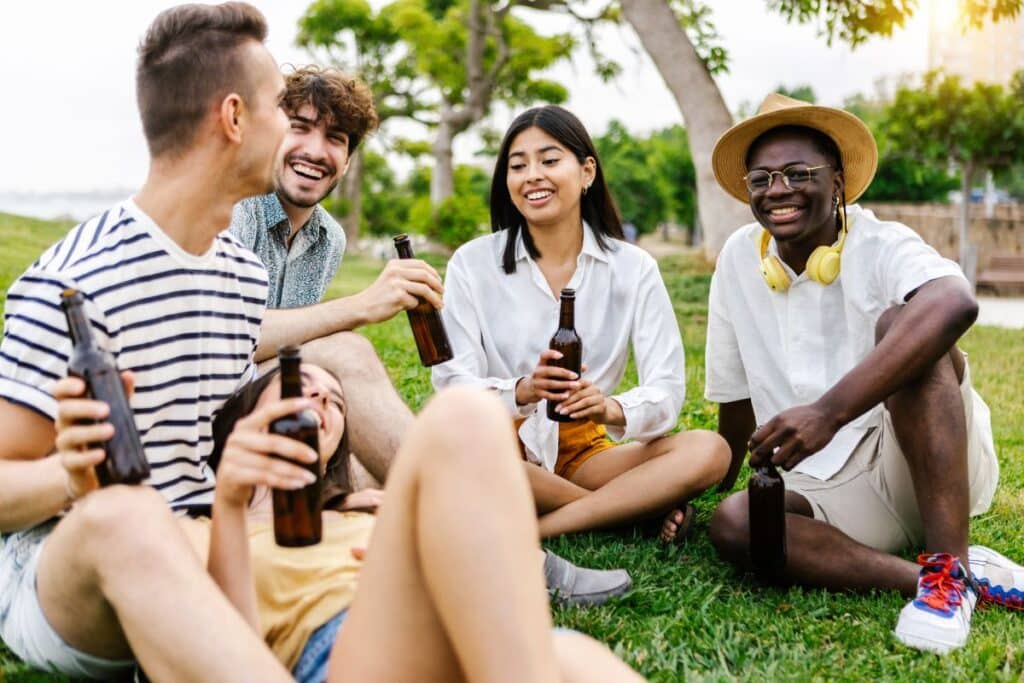 young group of diverse best friends hanging out in city park while drinking beer