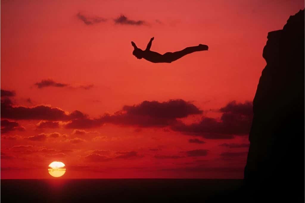 amazing shot of a high cliff diver in midair with stunning sunset in the background