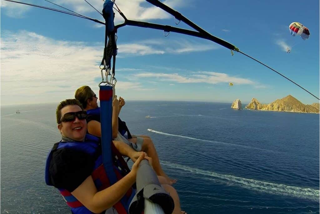 man holding a selfie stick while parasailing in the air with a friend